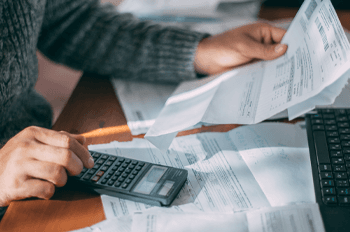 Person sitting at a desk using a calculator while looking at their bills