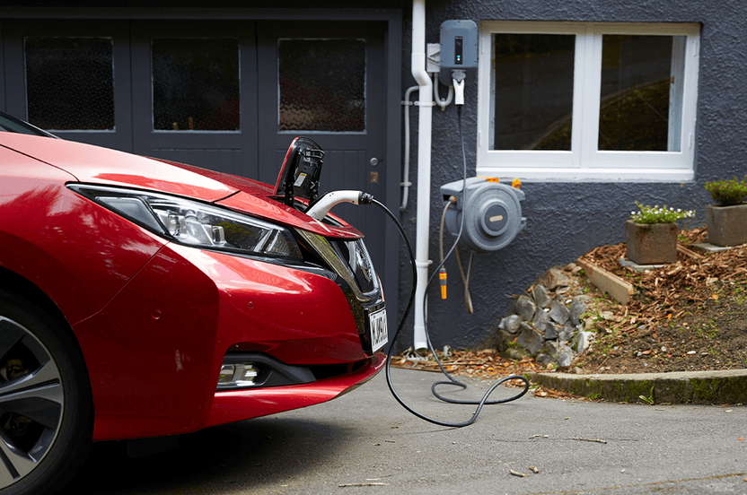 Red electric vehicle plugged in to home charger.
